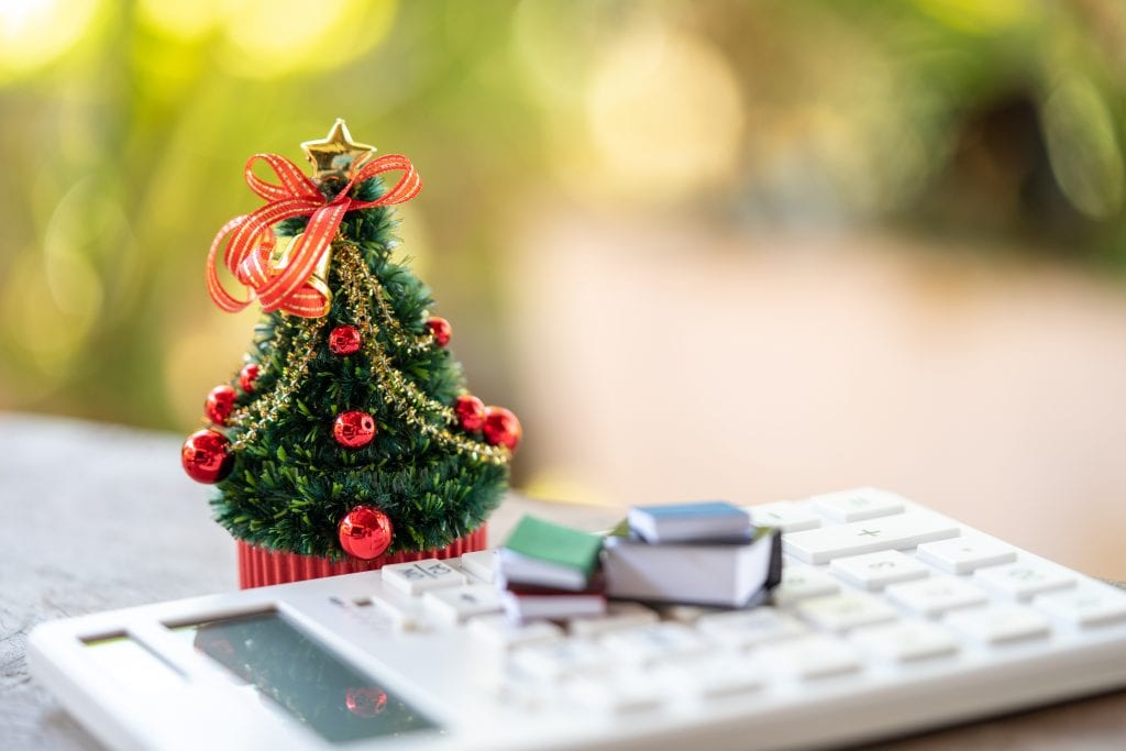 A beautifully decorated Christmas tree placed on a white calculator and with a miniature book.
