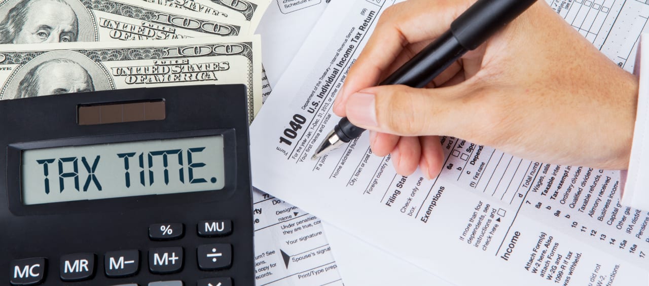 person filling out taxes with money and a calculator that reads tax time