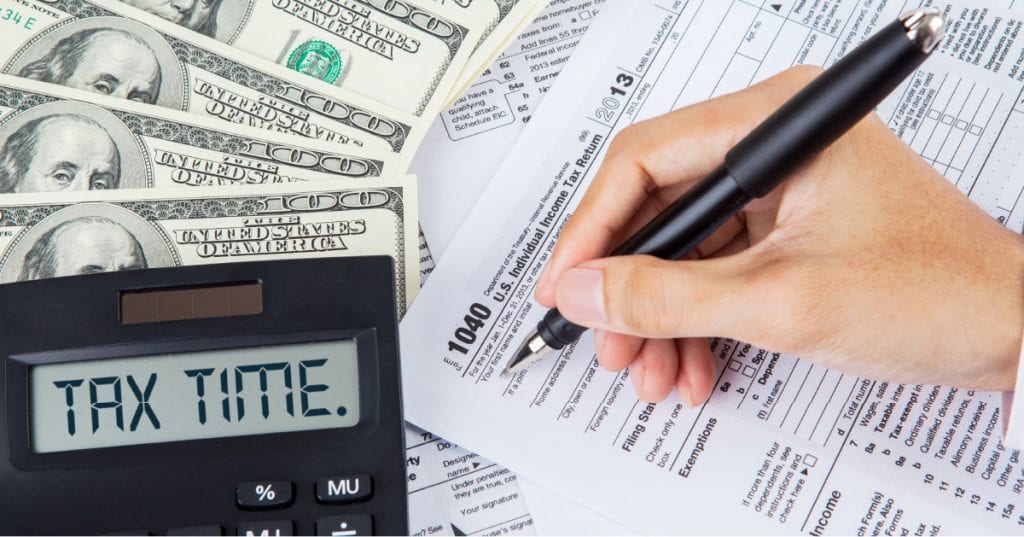 person filling out taxes with money and a calculator that reads tax time
